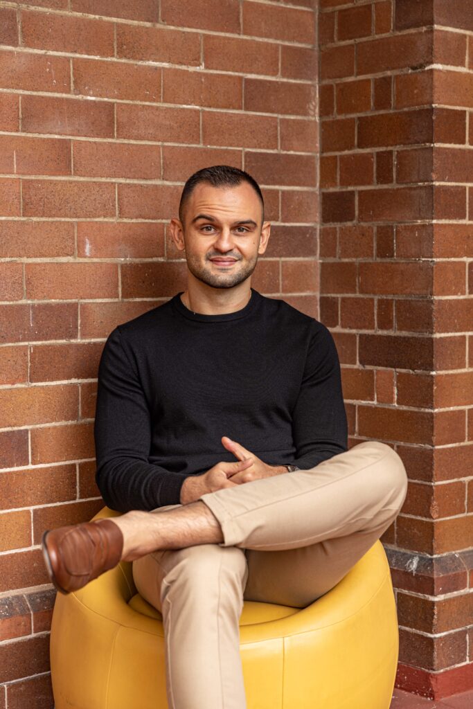 Marko Papuckovski sitting on a yellow chair in front of a red brick wall