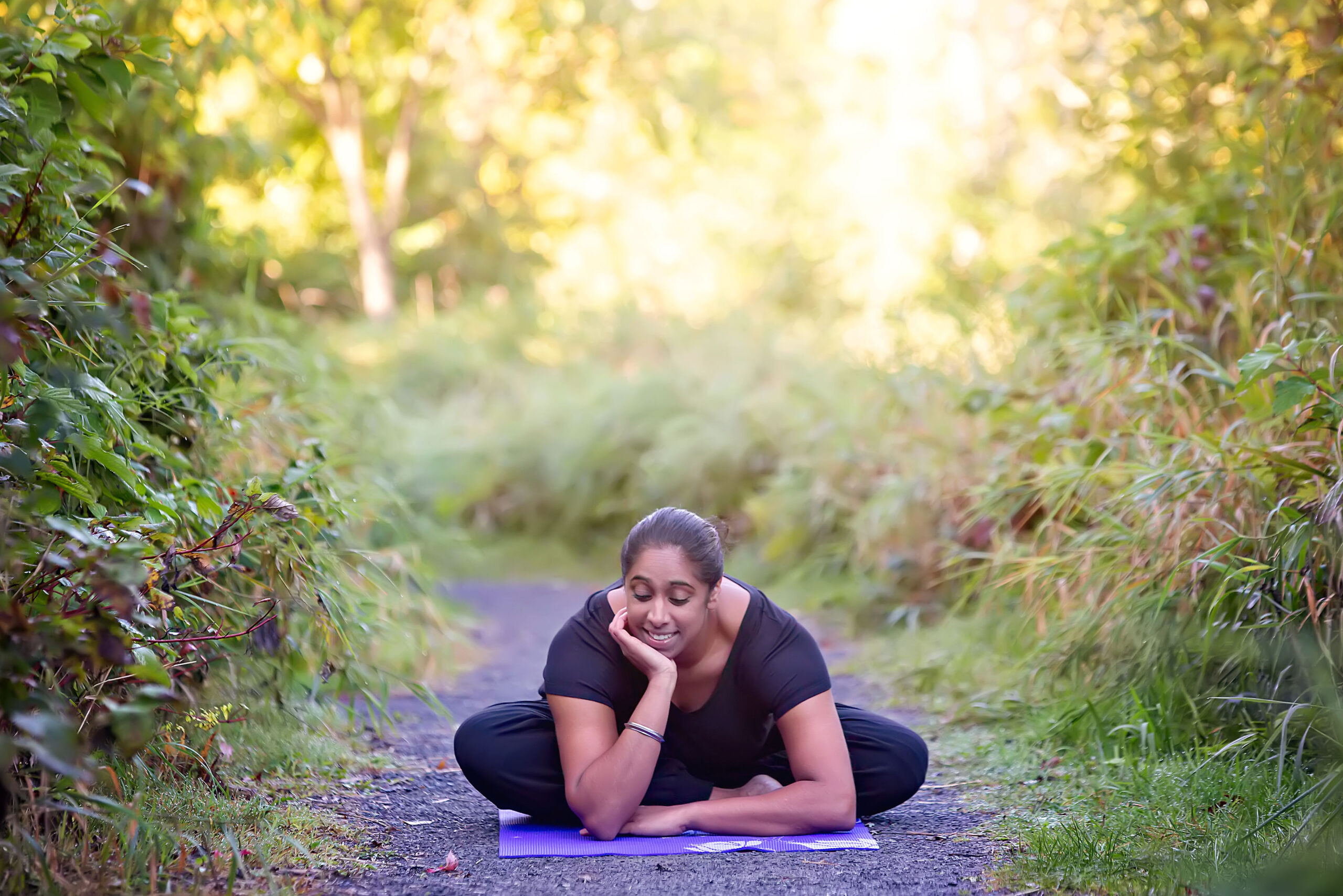 Jas sitting on a yoga mat in the middle of nature while smiling 